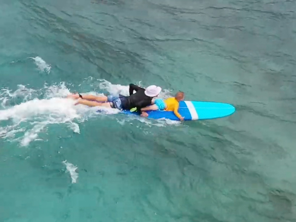 Child and instructor lying on board riding a wave